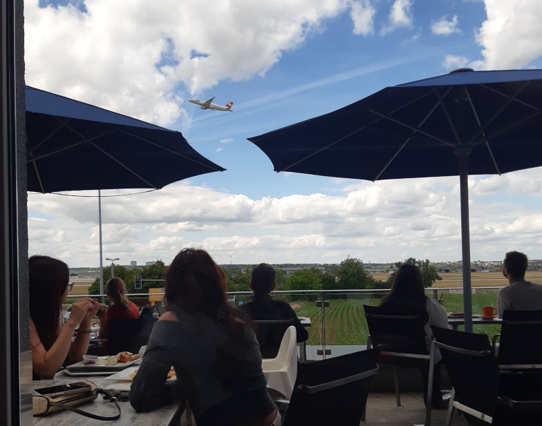 Gäste beobachten ein startendes Flugzeug von der Terrasse der Bäckerei Schill