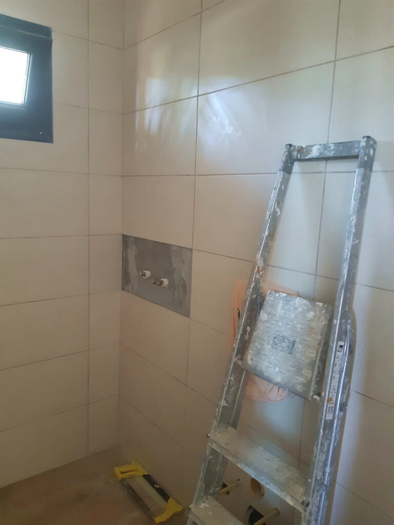 Gefliestes Badezimmer im Rohbau mit Leiter, Toilette und Waschbecken noch nicht angeschlossen