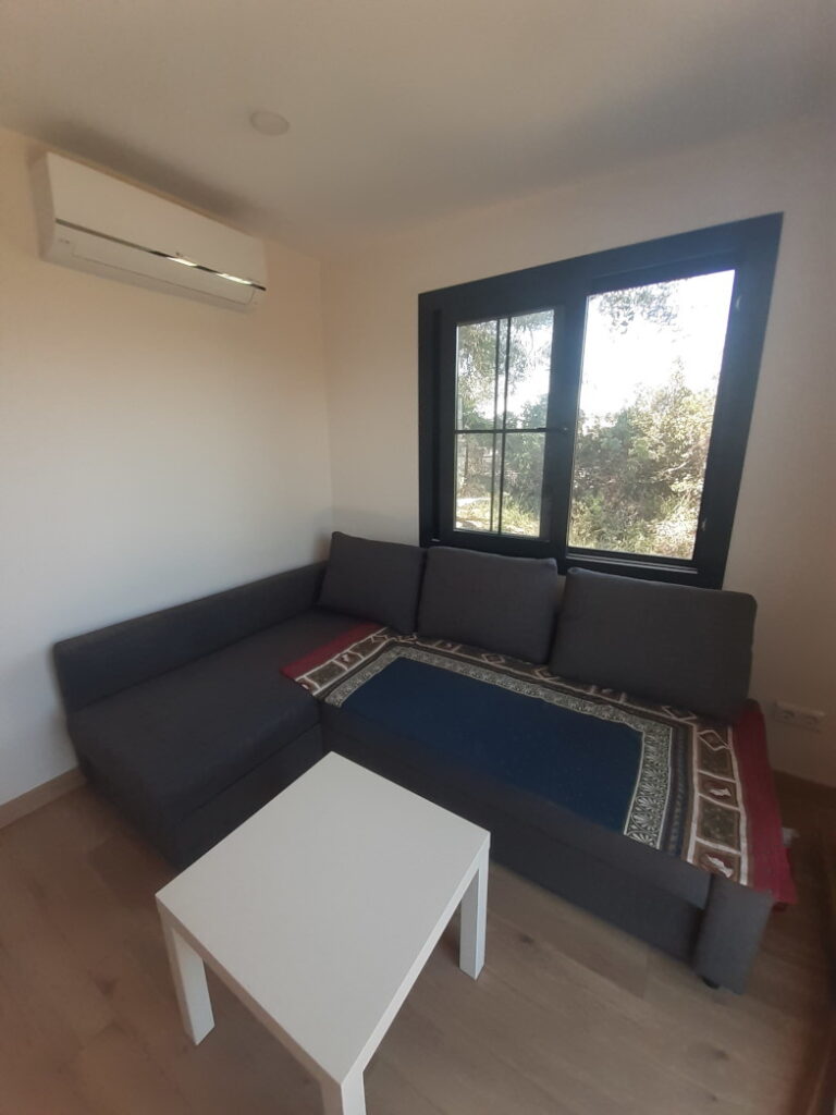 Wohnbereich im Tiny House mit Sofa, Couchtisch und großem Fenster mit Blick ins Grüne