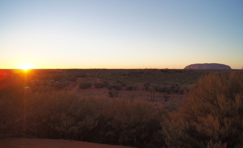 Der Uluru bei Sonnenuntergang, umgeben von rotem Spinifexgras im australischen Outback