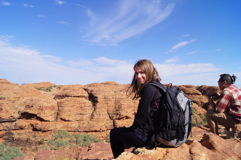 Frau sitzt mit Rucksack auf roten Felsen der Kata Tjuta während eines Ausflugs