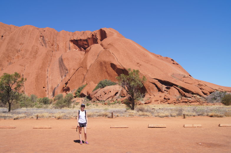 Person steht an der Felswand des Uluru während einer Wanderung
